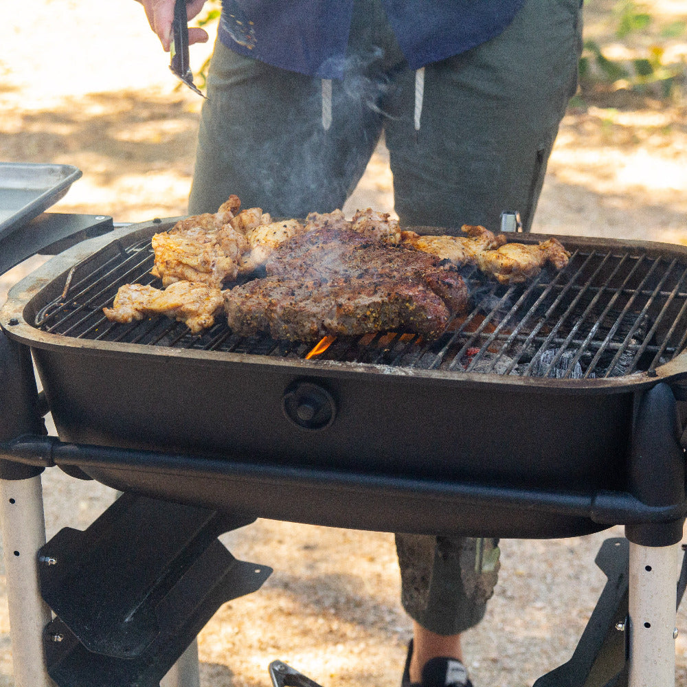 Person grilling meat on a portable grill outdoors