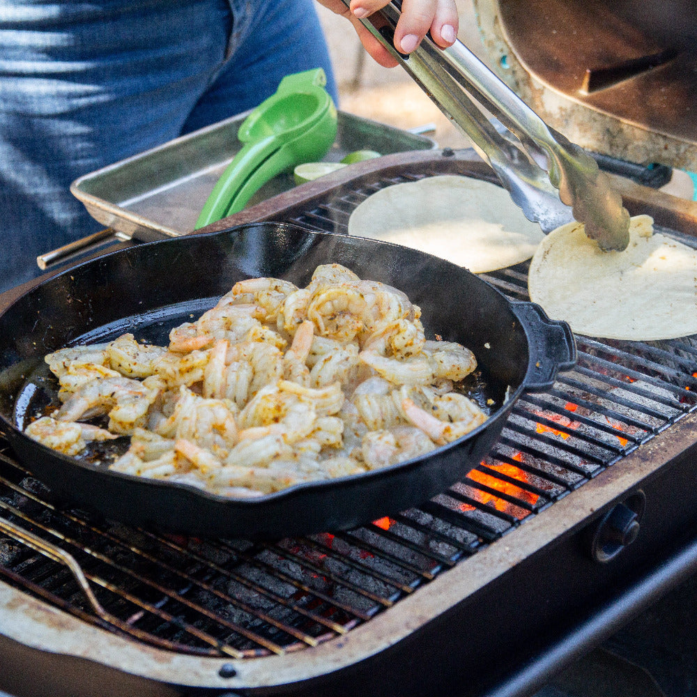 Person cooking on a grill with a cast iron skillet and tortillas.